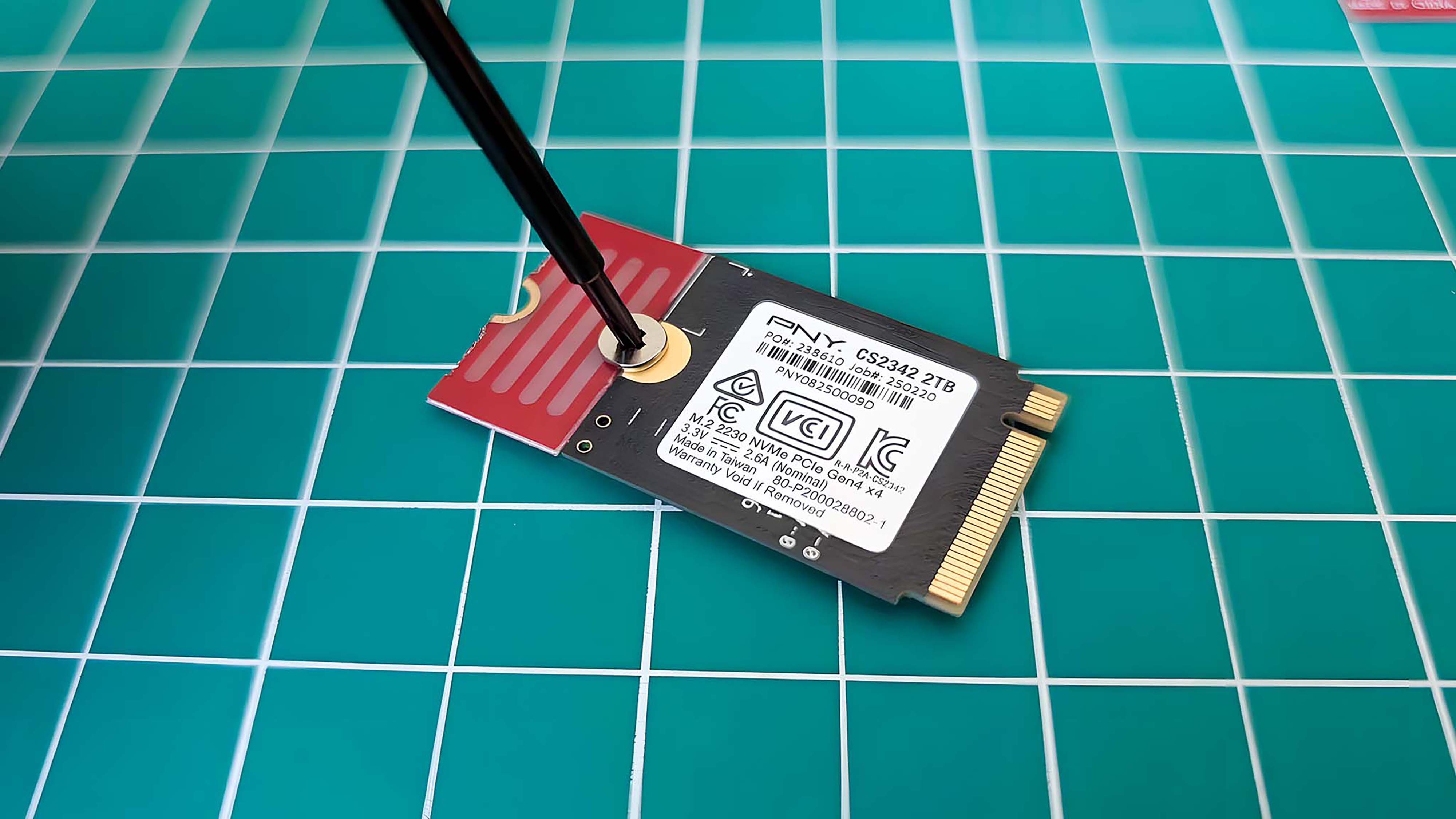 Отвертка прикручивает расширитель SSD к SSD.