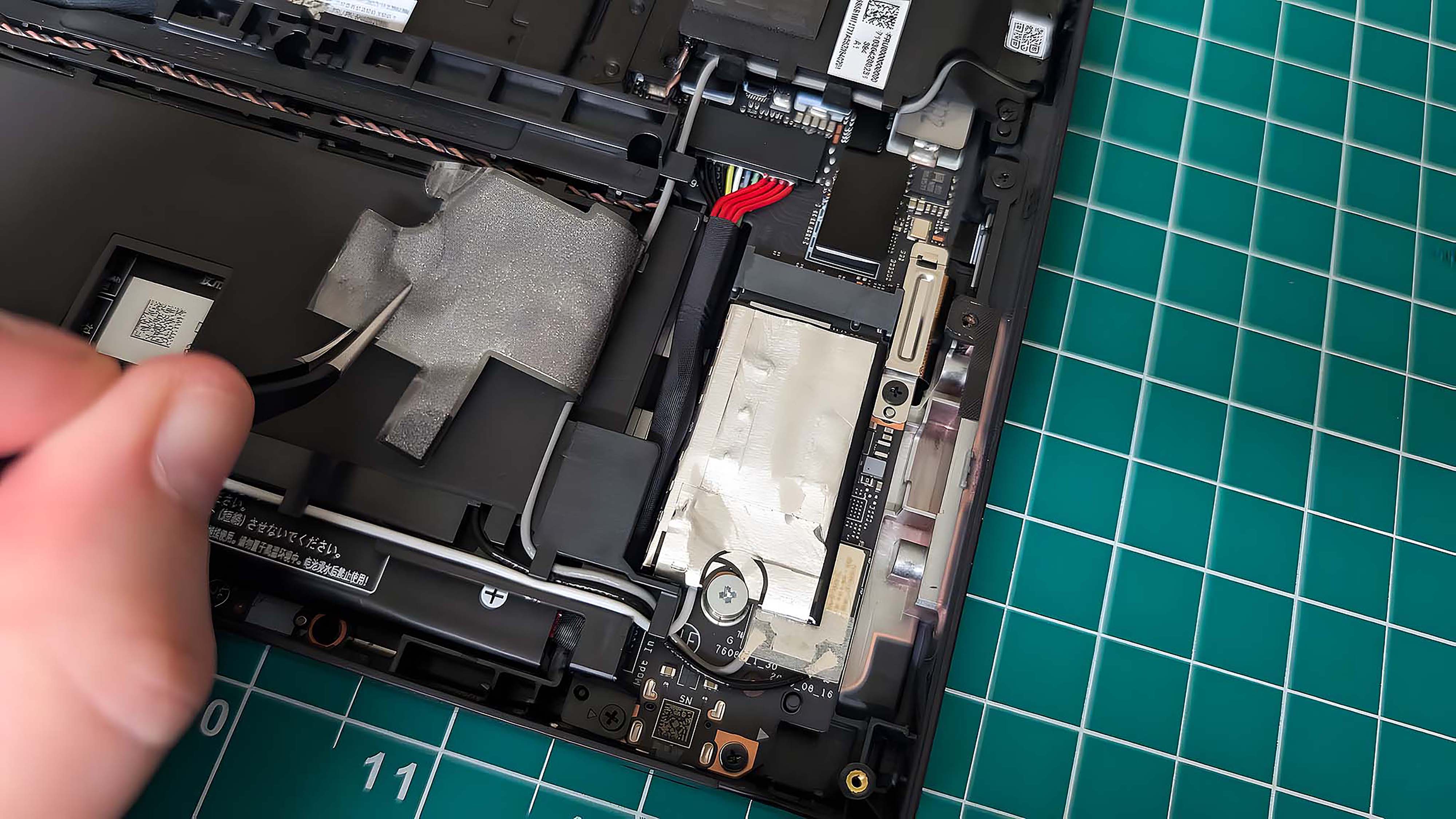 Рука пинцетом отклеивает наклейку аккумулятора от SSD Lenovo Legion Go.
