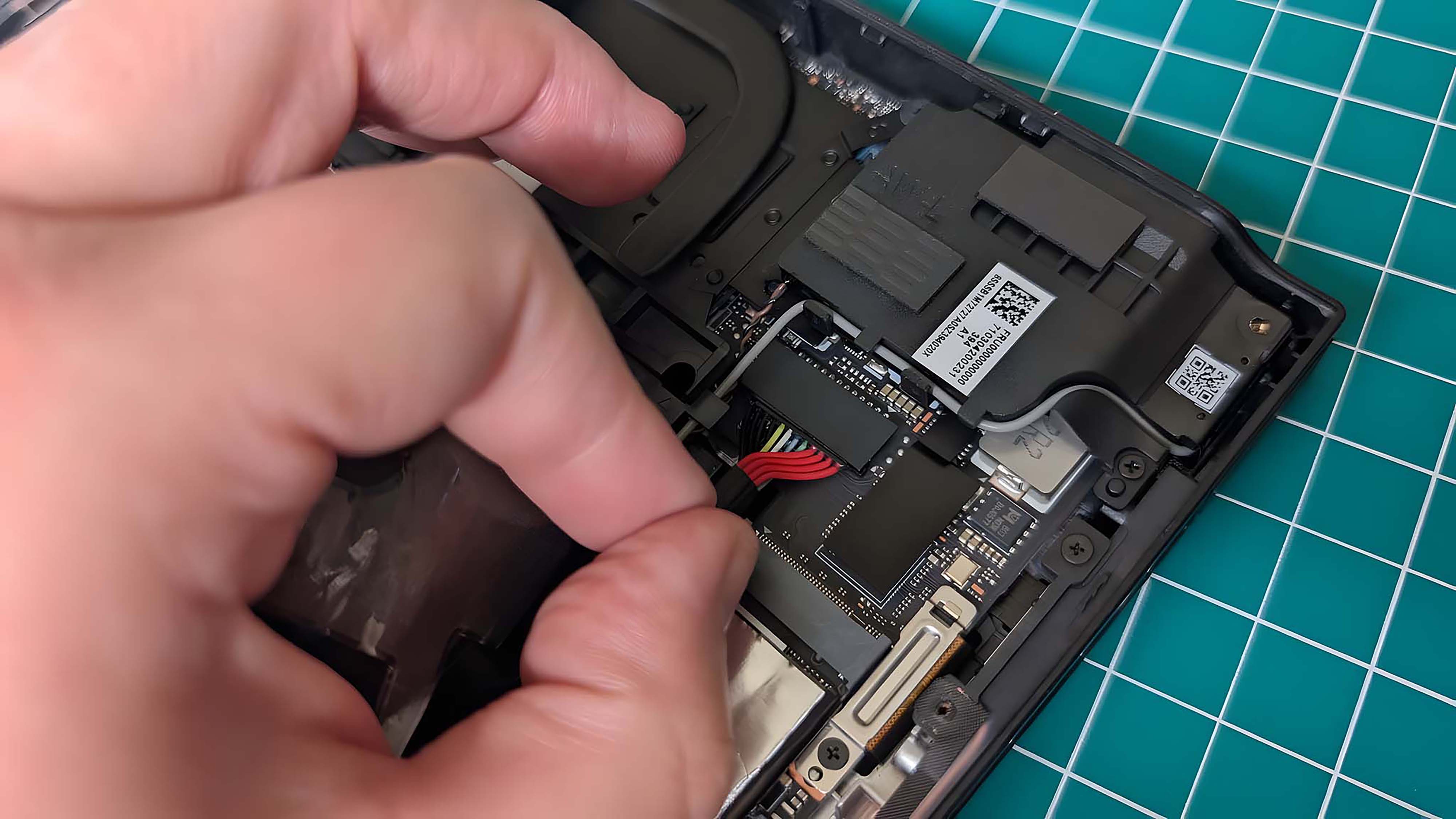 Палец и большой палец отсоединяют кабели аккумулятора Lenovo Legion Go.