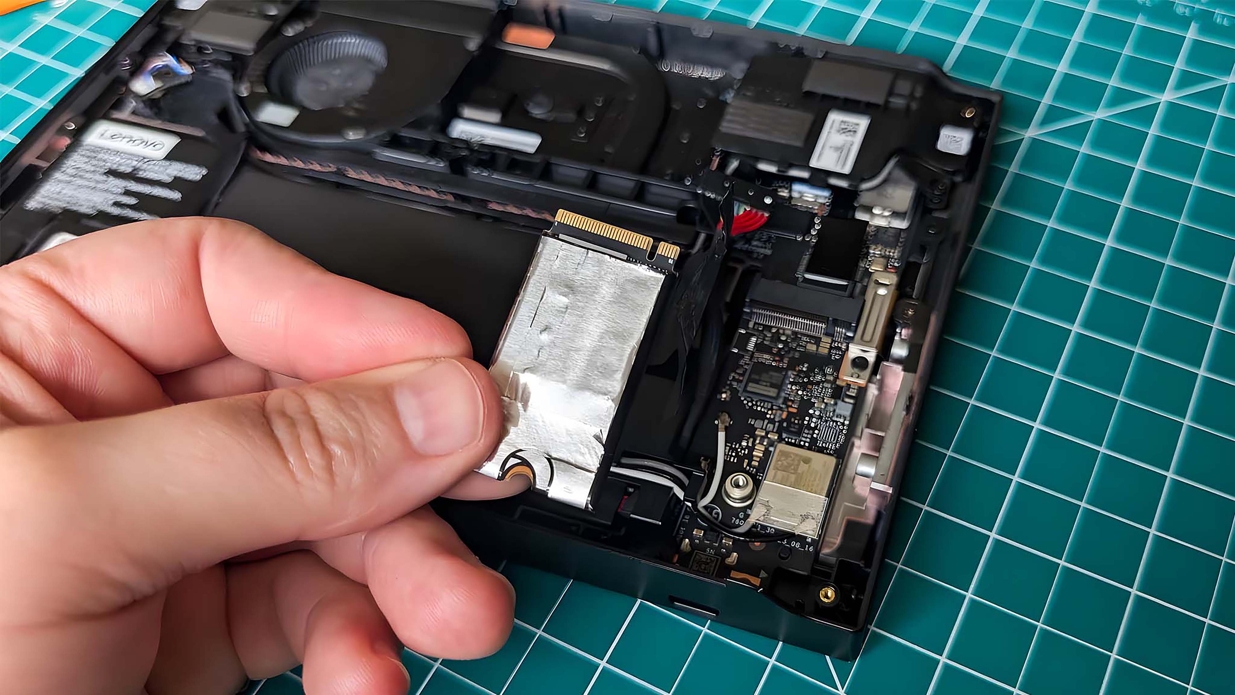 Рука держит оригинальный SSD Lenovo Legion Go над портативной консолью.