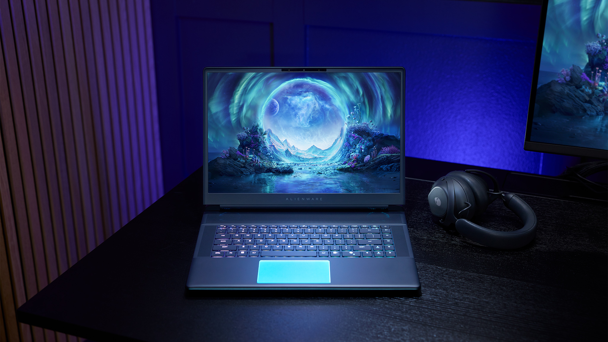 An Alienware Area-51 Laptop on a desk next to a headset and a gaming monitor.