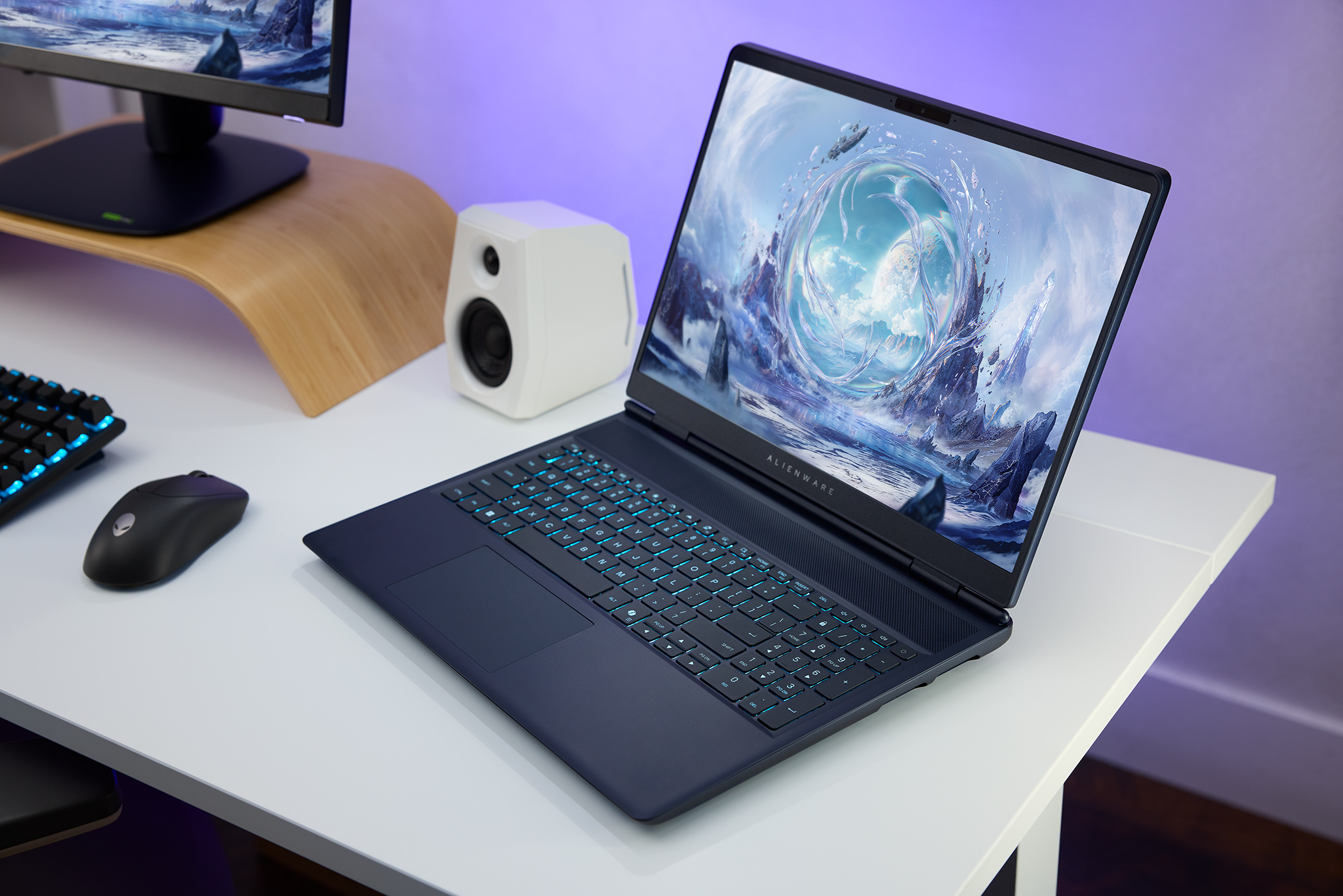 Alienware 16X Aurora laptop on a white desk next to a gaming mouse, gaming keyboard, and speakers.
