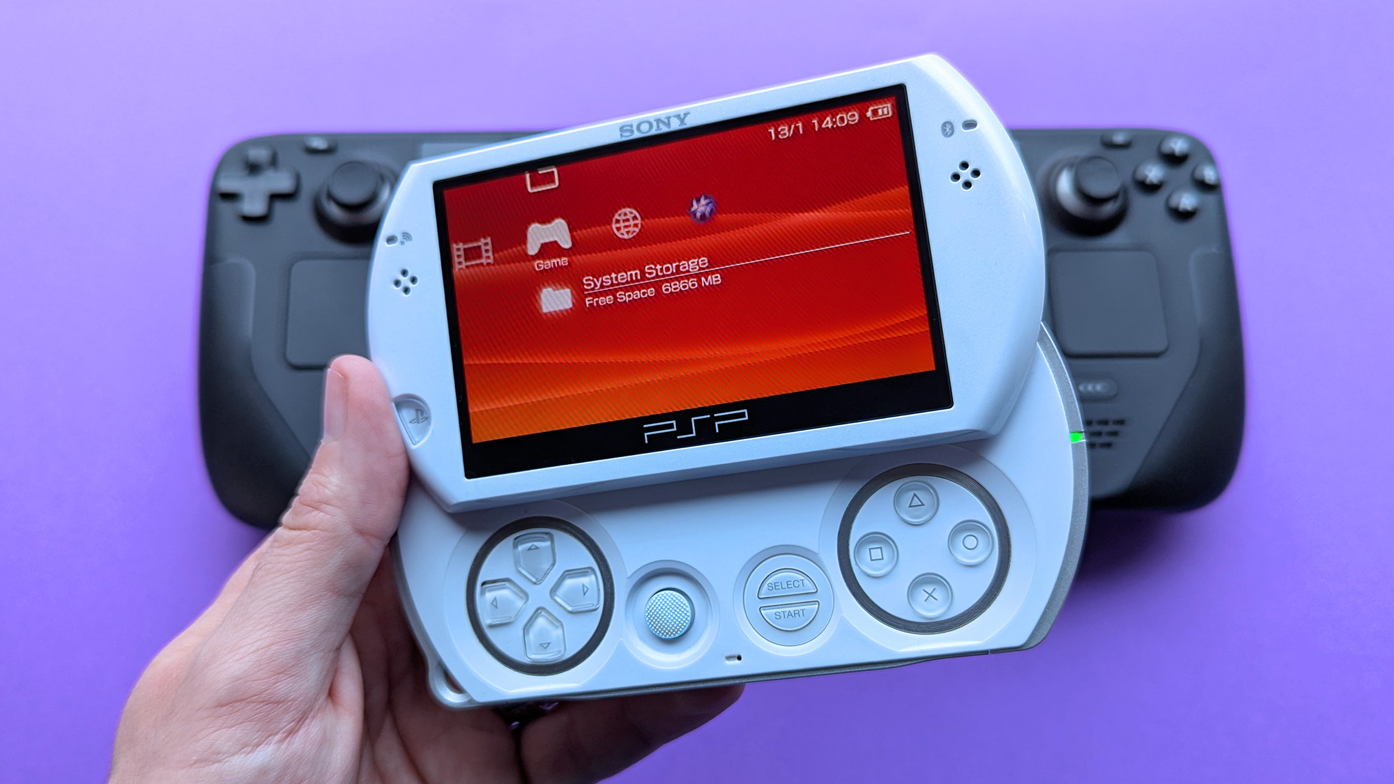 Sony PSP Go handheld resting above a Steam Deck on a purple card stock background