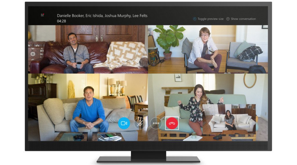 A video call with four participants displayed on a TV screen, each in their own home setting. They all appear relaxed and engaged.