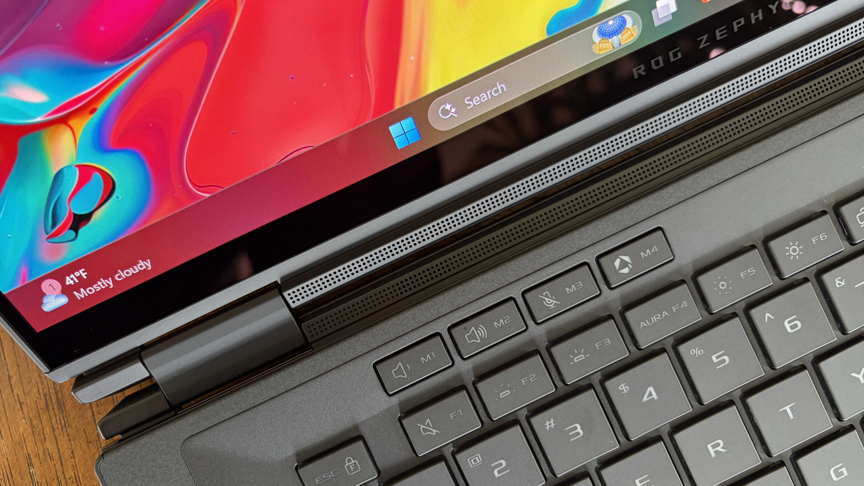 A close-up of a laptop displaying a colorful screen with swirling colors. The keyboard and part of the metal hinge are visible. The taskbar shows a partly cloudy weather icon and a temperature of 41°F. The overall tone is vibrant and modern.
