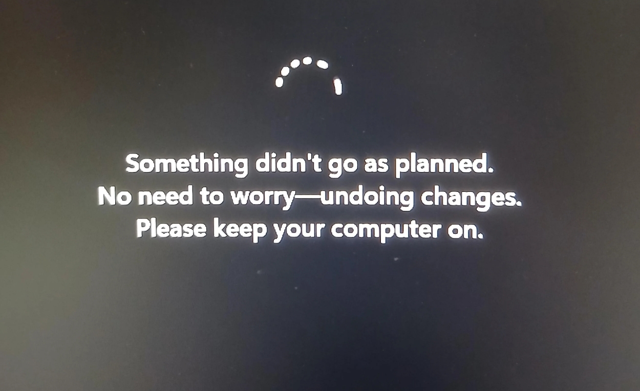 A computer screen displays a message: "Something didn't go as planned. No need to worry&ndash;undoing changes. Please keep your computer on." A loading circle is shown above.
